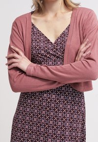 Rosa färgad kort cardigan över en djupt mönstrad klänning med geometriska former i marinblått, burgundy och kräm. Mjuk textur med långa ärmar.