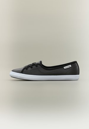 Sneaker Lacoste nera low-top con suola bianca, lacci neri e targhetta con logo sul lato su sfondo neutro.