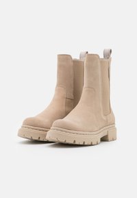 Béžové semišové kotníkové boty s elastickými bočními panely, silnou gumovou podrážkou a poutky na zadní straně pro snadné obouvání. Strukturální povrchová úprava.