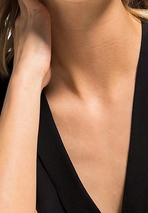 Vêtement noir avec un décolleté en V, texture lisse, avec la peau visible au niveau du cou et de l'épaule. Main reposant près du cou.