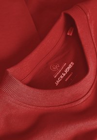 Red cotton T-shirt with a ribbed crew neck. Features a tag with “JACK & JONES” branding and “recycled cotton” detail. Soft texture.