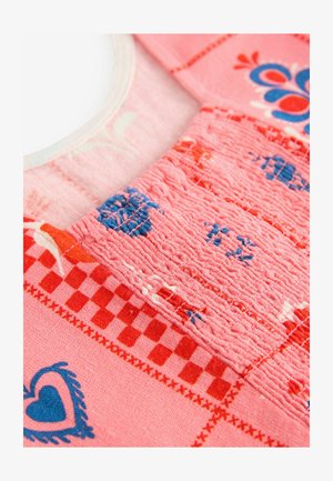 Tissu à motifs roses présentant une zone texturée avec des motifs rouges, bleus et blancs, y compris des cœurs et des designs à carreaux. Matériau doux.