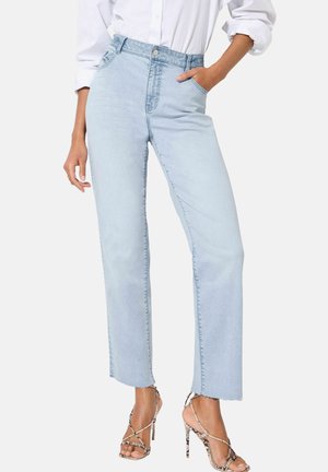 Jean taille haute bleu clair, à coupe droite, avec poches frontales et ourlet effiloché, associés à des sandales à talons hauts à lanières.