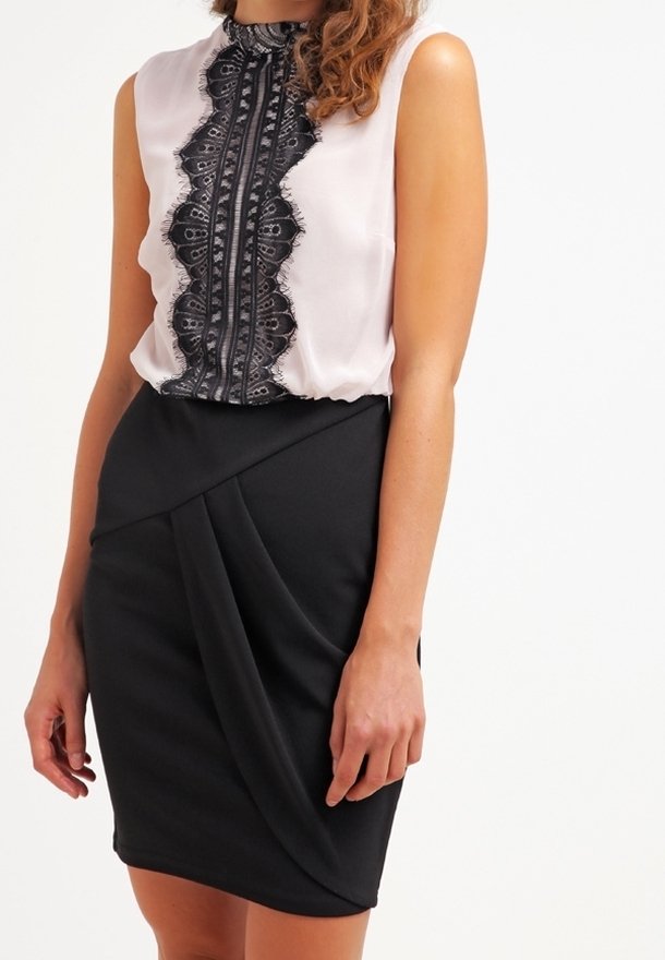 Černá sukně s drapovanými detaily v kombinaci s světle růžovým topem bez rukávů, který má černé krajkové ozdoby a vysoký stojáček.