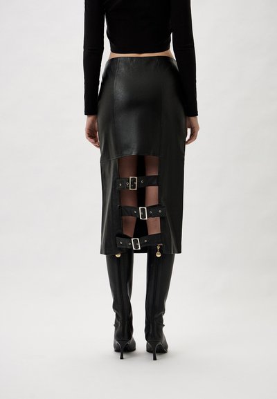 Black leather skirt with side cutouts and buckle accents. It features a fitted design and is paired with high, glossy black boots.