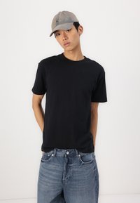 T-shirt in cotone nero a maniche corte abbinato a jeans in denim azzurro chiaro. Il modello indossa un cappellino da baseball grigio con un piccolo logo.