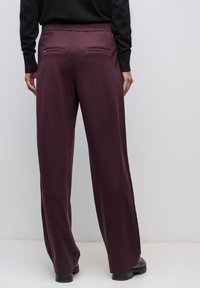 Burgundské kalhoty se širokými nohavicemi a elastickým pasem, vybavené dvěma zadními kapsami a hladkou, texturovanou tkaninou.