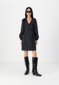 Robe noire avec un motif texturé noir, décolleté en V, manches bouffantes, et bottes noires brillantes jusqu'aux genoux avec un effet peau de crocodile.