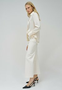 Camisa de manga larga de color crema con rayas verticales, combinada con pantalones de pierna ancha blancos y tacones de tira negra con punta. Textura de tela suave.