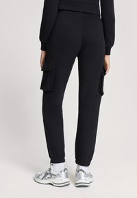 Czarne spodnie dresowe ze zwężanymi mankietami, z dwoma kieszeniami naszytymi po bokach, wykonane z miękkiego materiału, w połączeniu z srebrnymi butami sportowymi i białymi skarpetkami.