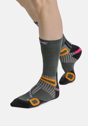 Twee benen met grijze sportsokken met oranje, roze, zwarte en witte designelementen, afgebeeld tegen een witte achtergrond.