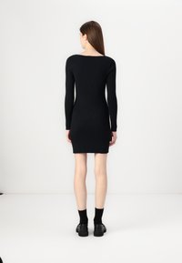 Robe noire à manches longues à côtes, décolleté carré, coupe près du corps, longueur genou, accompagnée de chaussettes noires et de chaussures chunky.