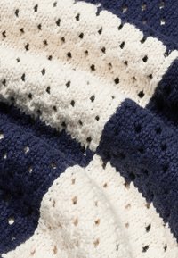 Gestrickte Überwurffdecke mit abwechselnden Abschnitten in Marineblau und Creme, einem strukturierten Muster und offenem Gewebe, verziert mit kleinen schwarzen Punkten.