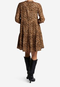 Vestido de estampado de leopardo en tejido ligero, con falda de volantes, mangas largas y cuello redondo. Combinado con botas negras hasta la rodilla.