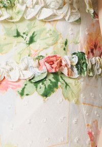 Tissu à motifs floraux avec de petits pois texturés, orné d'un bord volanté pastel aux teintes vertes et roses, mettant en valeur un design vintage.