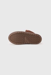 Suela de zapato de goma marrón con un patrón texturizado, que presenta un logo triangular en el talón y un borde reforzado para mayor durabilidad.