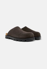 Mörkbruna mocka tofflor med rund tå och en texturerad svart gummisula. Har en minimal design med en vadderad beige innersula.