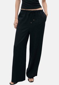 Black wide-leg pants with a relaxed fit, drawstring waist, and wooden bead accents. Made of soft, lightweight fabric with no patterns.