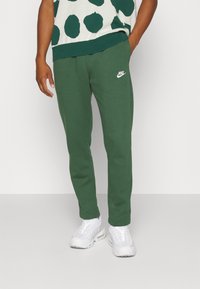 Gröna Nike sweatpants i mjukt tyg, smal passform, med resårmidja som har en vit logotyp på vänster lår.