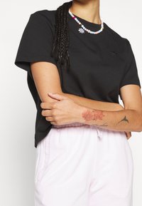 Svart bomulls-t-shirt med korta ärmar och rund halsringning. Har ett färgglatt pärlhalsband och ljusrosa byxor med snörning och fickor.