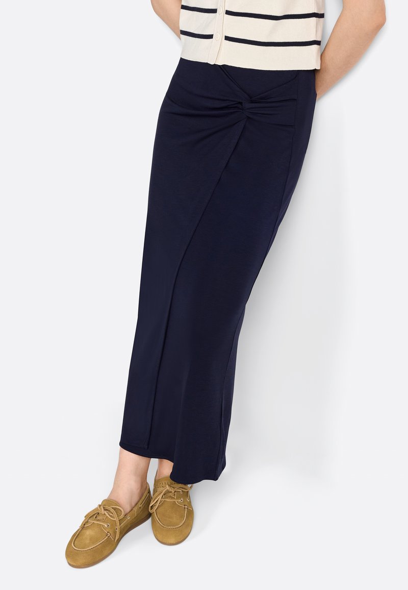 Gonna maxi blu navy con un dettaglio annodato davanti, realizzata in tessuto morbido. Abbinata a scarpe beige con lacci per un look casual.