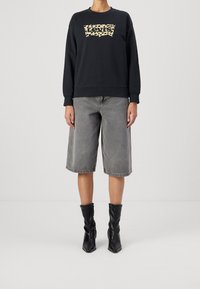 Felpa nera con logo Levi's a stampa leopardata, abbinata a shorts di jeans grigi lunghi fino al ginocchio. Il modello indossa stivaletti neri a ruches.