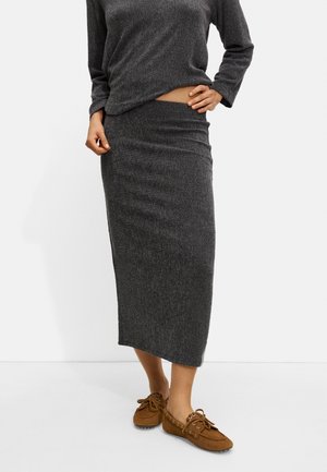 Jupe midi gris en maille côtelée avec un design ajusté, assortie à des mocassins marron en cuir souple. Le tissu semble texturé et extensible.