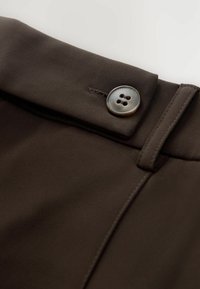 Pantaloni in tessuto marrone con chiusura frontale a bottoni a quattro fori, superficie liscia e cuciture dettagliate lungo le cuciture.