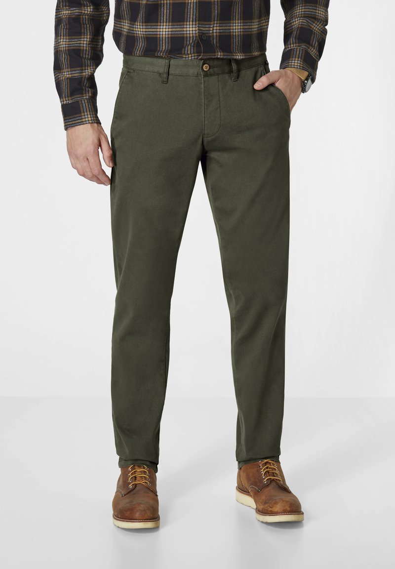 Olive green cotton chinos with a straight cut, button closure, side pockets, and a matte finish, complemented by brown leather boots.