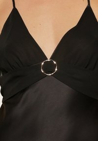 Robe noire avec un décolleté en V, présentant une taille tordue et un accent circulaire métallique au centre. Texture de tissu lisse.