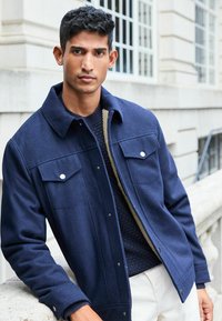 Navy blue wool jacket with two chest pockets, snap buttons, and a textured lining. Layered over a navy knit sweater.