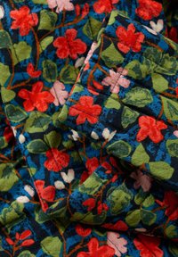 Tissu matelassé avec un motif floral composé de fleurs rouges, roses et vertes sur un fond bleu foncé. Matériau en coton texturé et doux.