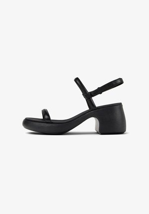 Schwarze Absatzsandalen mit offenem Zeh und Knöchelriemen. Aus glattem Leder mit einem klobigen, strukturierten Absatz und einem geschwungenen Sohlen-Design.
