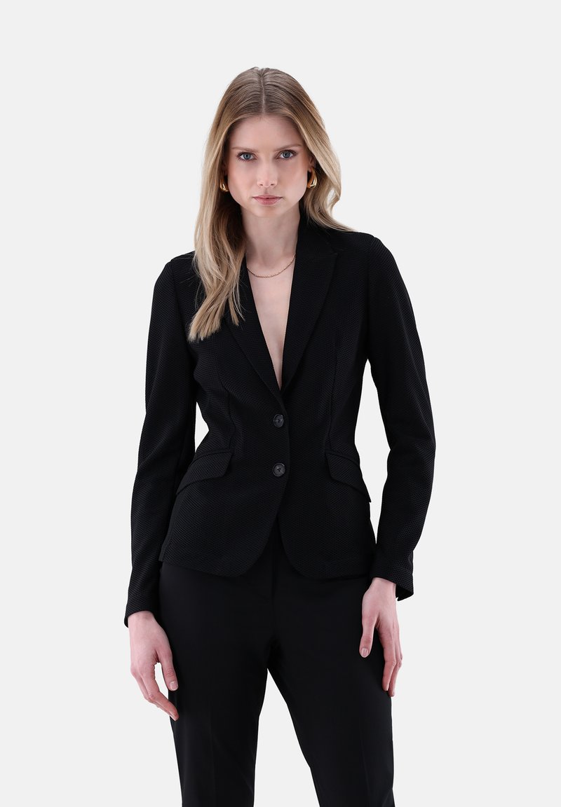 Schwarzes Blazer mit angepasstem Design, strukturiertem Stoff, zwei Knöpfen und spitzen Revers. Kombiniert mit maßgeschneiderten schwarzen Hosen für einen formellen Look.