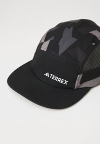 Sort og grå kasket med fladt skygge, prydet med et geometrisk mønster, netpaneler i siden og en hvid "TERREX" logo foran.