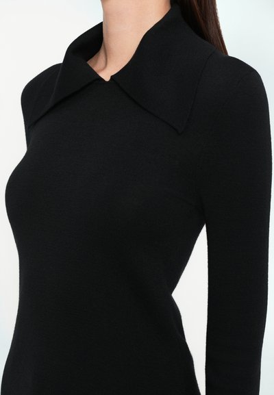 Svart strikket genser med stor, brettet krage, slim fit og lange ermer. Glatt tekstur og minimalistisk design.