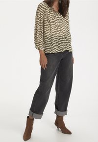 Blouse légère et semi-transparente avec un motif vert abstrait, associée à un jean sombre et ample ainsi qu'à des bottines marron.