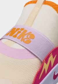 Krémovo ružová teniska Nike s oranžovým logom na elastickom remienku a žltým detailom blesku na ružovej časti podrážky.