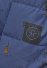 Blå pufferjacka i tyg med små färgglada skidgrafik och en svart logotypflik. Texturerad, vadderad design med synlig sömnad.