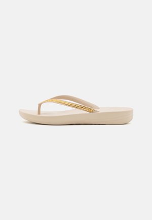Sandale en tongs beige avec une semelle texturée, dotée d'une sangle accentuée de strass jaunes et d'un design minimaliste.