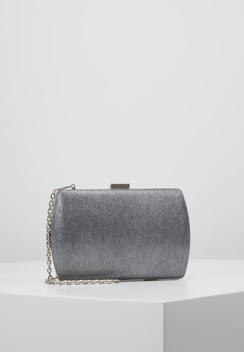 Pochette rectangulaire argentée avec un léger éclat, fermoir métallique et bandoulière chaîne argentée attachée, présentée sur une surface blanche.