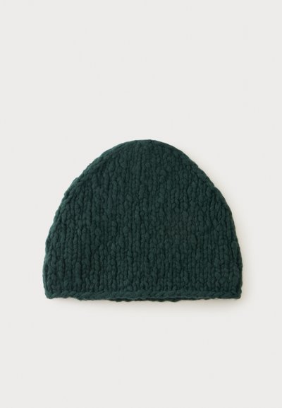 Bonnet en laine épaisse tricotée vert foncé avec un motif texturé, posé à plat sur un fond blanc.
