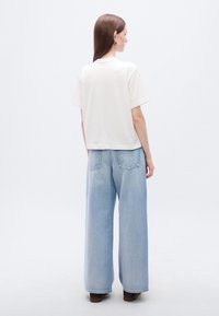 Λευκό βαμβακερό T-shirt με κουτίκο κόψιμο, σε συνδυασμό με ανοιχτό μπλε τζιν παντελόνι με φαρδιά πόδια, με ορατές ραφές και πίσω τσέπες.