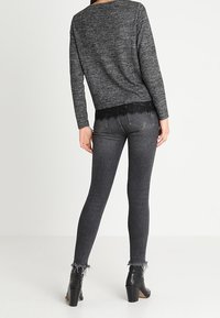 Černý texturovaný svetr s krajkovým zdobením na lemu, kombinovaný s tmavě šedými úzkými džínami s třepícími se lemy u kotníků a černými botami na podpatku.