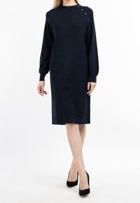Marineblaue Strickkleid mit langen Ärmeln, hohem Kragen und Knopfdetails an den Schultern. Verfügt über eine gerade Silhouette und reicht bis unter das Knie.