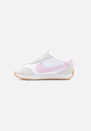 Baskets blanches et gris clair avec un swoosh Nike rose, une semelle gomme et une languette rose à l'arrière, vues de profil sur un fond uni.