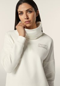 Sweatshirt bianco con collo alto ripiegato e texture morbida. Presenta la scritta "FREDDY TRAINING" ricamata in argento sul petto.