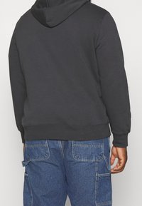 Sweat à capuche noir avec une texture douce, doté d'une poche kangourou et de poignets côtelés. Associé à un pantalon cargo en denim bleu avec des poches latérales.