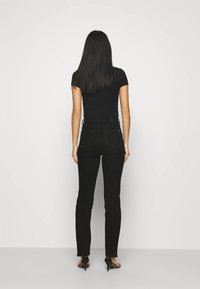 Černé vyšší džíny s přiléhavým střihem, které mají klasický pět pockets design a detail na zadní části. Jsou nošeny s černým topem.