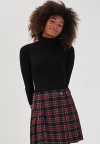 Sort ribbet turtleneck med tætsiddende design. Matchet med en ternet plisseret nederdel i sort, rød og hvid, der har en frontlås og knapper i siden.